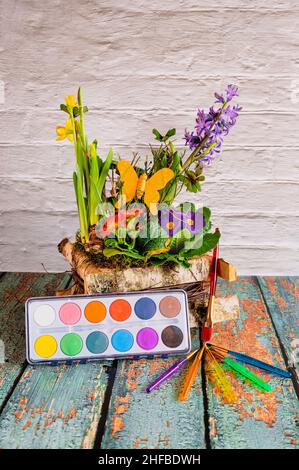 Graziosa disposizione di vari fiori di primavera colorati con decorazioni, una scatola di vernice e pennelli. Foto Stock