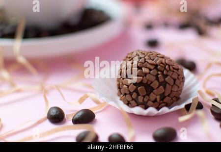 Caramelle al cioccolato al tartufo su sfondo rosa con chicchi di caffè sparsi e una tazza bianca con caffè sullo sfondo. Foto di alta qualità Foto Stock