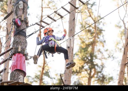 La bambina è in piedi su una corda, tenendo una corda con le mani. Un bambino in un parco funi supera gli ostacoli Foto Stock