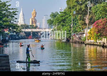 Giovani in canoa a Klong Bangkok Yai, un canale a Thonburi, Bangkok, Thailandia, Thonburi; b/g: Il Buddha gigante di Wat Paknam Phasi Charoen Foto Stock
