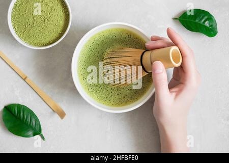 Tè verde Matcha. La donna lancia il tè matcha su uno sfondo grigio in cemento. Cerimonia del tè giapponese. Vista dall'alto, piatto. Foto Stock