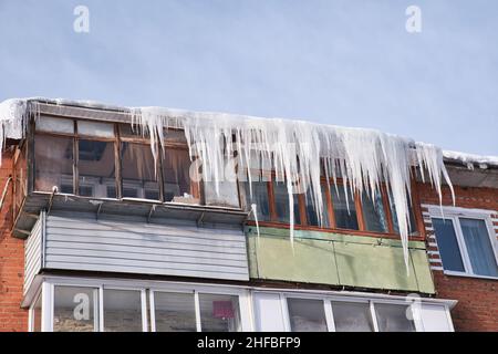 Balconi di una vecchia casa residenziale in mattoni coperti dalle enormi ghiacciole. Ghiaccioli pericolosi pende dal tetto. Inverno Nord duro in città. Foto Stock