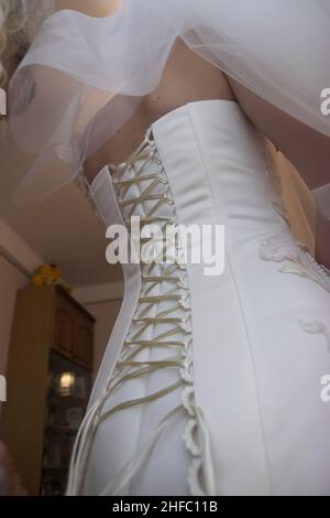 Il corsone della sposa in un abito da sposa lungo bianco è allacciato con un sottile nastro bianco. Nastro unbound sul corsetto della sposa il giorno del matrimonio. Foto Stock