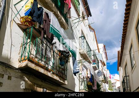 Molti vestiti appesi ai balconi nelle strette stradine del quartiere di Alfama, Lisbona, Portogallo. Tipico stile di vita tradizionale semplice nel vecchio Foto Stock