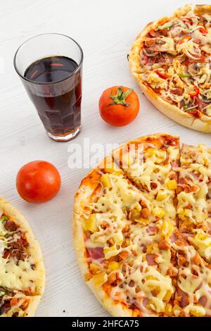 tavolo del ristorante servito con pizze di ingredienti diversi, bicchiere con soda e decorato con pomodori, cibo e bevande in studio Foto Stock