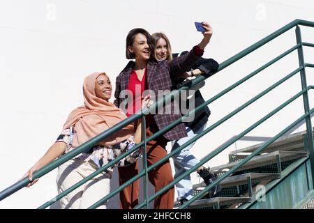 Allegre girlfriends multirazziali che prendono selfie su smartphone su scale Foto Stock