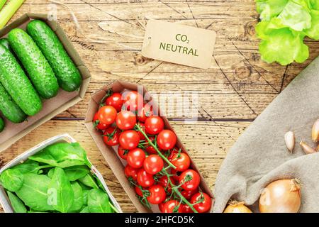 Composizione alimentare vegana sana con verdure locali, agricole in imballaggi eco-compatibili con un'etichetta con la scritta carbonio neutro su un dorso di legno Foto Stock