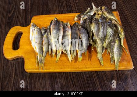 Il pesce salato secco si trova sul bordo. Sfondo marrone. Foto Stock
