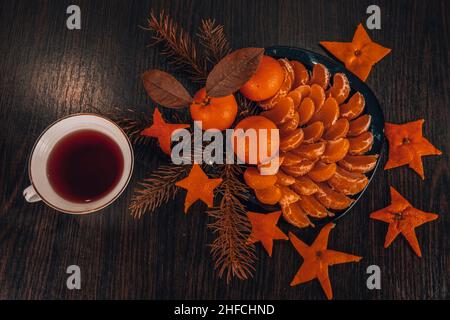 Vista dall'alto dei tangerini con foglie in decorazione natalizia con albero di Natale, arancio secco e bacche su vecchio tavolo di legno. Stile rustico scuro Foto Stock