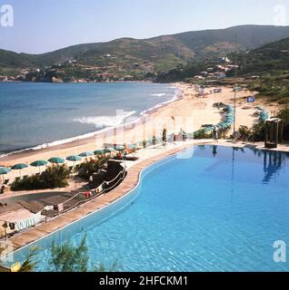 1960s, quadro storico e vista su un'inscricchiata baia dell'Isola d'Elba, con una graziosa e invitante piscina sul mare, con un'interessante piattaforma di immersione e tavola in legno. Foto Stock