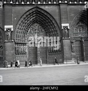 1950s, vista storica delle persone che camminano sul marciapiede fuori dalle tre porte d'ingresso alla Cattedrale medievale di Notre Dame, Parigi, Fance. Famosa per la sua architettura gotica, in quest'epoca l'esterno della cattedrale era coperto di sporcizia o fuliggine. Foto Stock