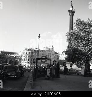 1960s, accanto ad un ingresso alla metropolitana di Londra, diversi taxi di Londra si accingono alla rotatoria di Trafalgar Square, Westminster, Londra, Inghilterra, Regno Unito. La famosa statua, la colonna di Nelson, domina lo skyline. Foto Stock