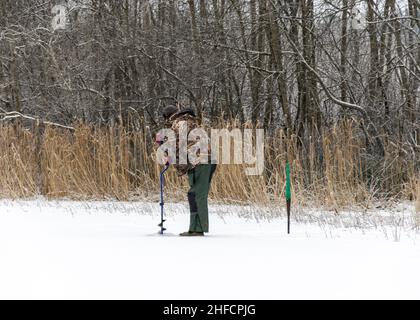 Un uomo di pesca del ghiaccio del solone siede su un lago nevoso e cattura il pesce. Attività invernali. Foto Stock