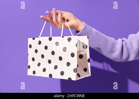 Womans mano che tiene carta bianca shopping borsa su sfondo viola. Concetto di consegna della vendita dello shopping Foto Stock