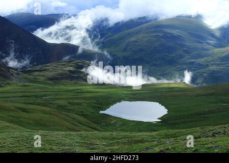 Lago in una valle con pendii di montagna, fiume e nuvole in estate all'alba Foto Stock