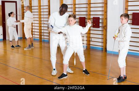 Istruttore di scherma con giovani recinti in aula di formazione Foto Stock