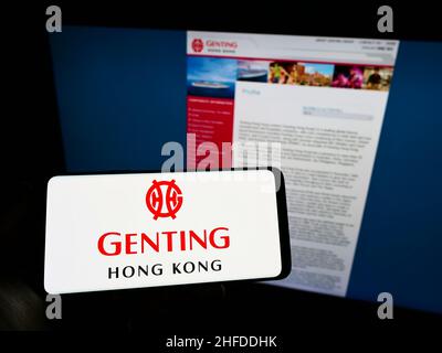 Persona che tiene smartphone con il logo della società turistica Genting Hong Kong Limited sullo schermo di fronte al sito web. Mettere a fuoco sul display del telefono. Foto Stock