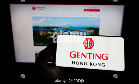 Persona che detiene il telefono cellulare con il logo della società turistica Genting Hong Kong Limited sullo schermo di fronte alla pagina web aziendale. Mettere a fuoco sul display del telefono. Foto Stock