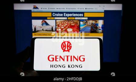 Persona che tiene il cellulare con il logo della società di turismo Genting Hong Kong sullo schermo di fronte alla pagina web Star Cruises. Mettere a fuoco sul display del telefono. Foto Stock