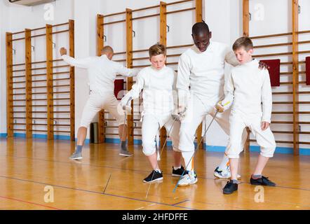 I ragazzi incentrati ascoltano attentamente il allenatore professionale di scherma in palestra Foto Stock