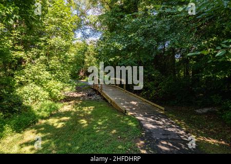 Un sentiero suburbano passerella con un ponte di legno su un torrente. Foto Stock