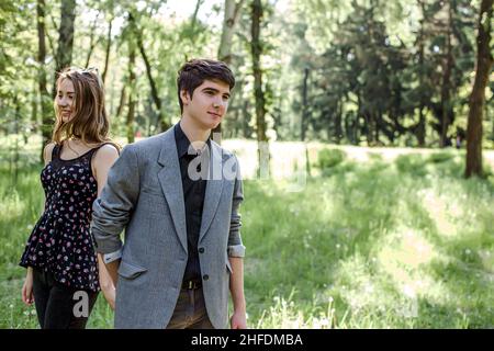 Il ragazzo guida la ragazza per mano. Una coppia innamorata cammina in un parco primaverile che tiene le mani. Una giovane famiglia felice trascorre del tempo insieme. Foto Stock