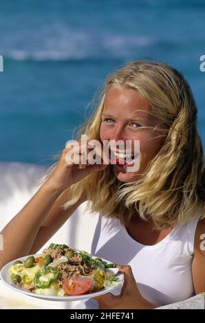 capelli biondi giovane donna ritratto bianco gonna naturale guardare fotocamera mangiare insalata piatto Foto Stock