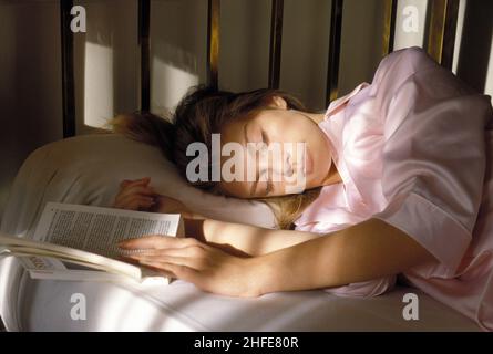 Bella bionda capelli bellezza dormire viso dormire nel letto ritratto profilo telecamera con morbido raggio di sole molto stanco libro aperto Foto Stock