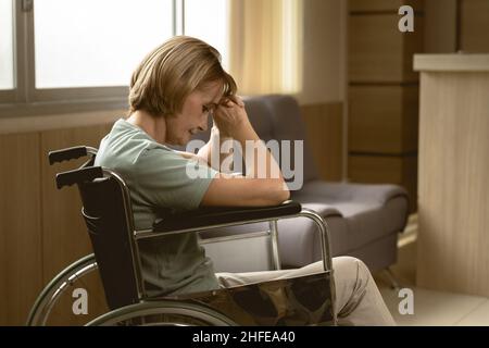 le donne adulte si sentono tristi solo seduti su sedia a rotelle alla luce soffusa della casa dell'ospedale Foto Stock