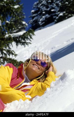 capelli biondi primo piano giovane donna ritratto stendere giù sulla neve sorridente guardando fotocamera anteriore alberi di natale sfondo Foto Stock