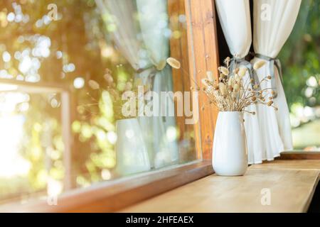 Tavolo in legno con decorazione a lato della finestra con vaso di fiori secchi nel cafe' Foto Stock