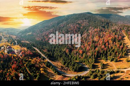 Alta vetta di montagna con foreste verdi e rosse e un colorato prato giallo sotto il cielo nuvoloso con vista panoramica del tramonto Foto Stock
