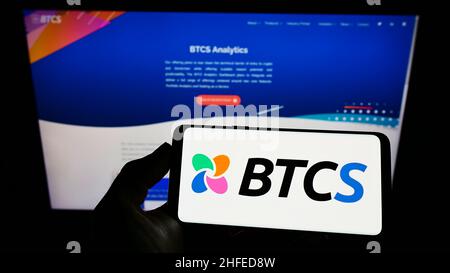 Persona che tiene il cellulare con il logo della società americana di blockchain BTCS Inc. Sullo schermo di fronte al sito web aziendale. Mettere a fuoco sul display del telefono. Foto Stock