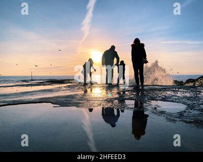 2022 0108 persone si divertono al tramonto sulla spiaggia di Camogli, Genova, Italia, nella stagione invernale, con una grande onda Foto Stock