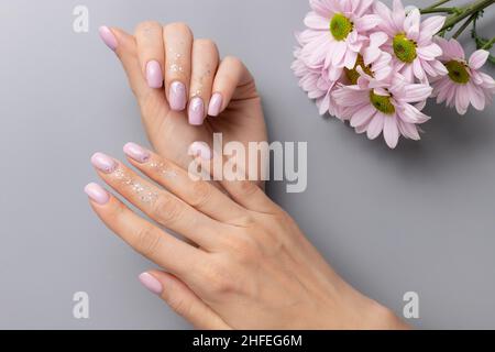 elegante manicure rosa con design in argento lucido su sfondo grigio Foto Stock