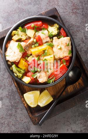 Stufato di pesce con verdure di stagione primo piano in una ciotola sul tavolo. Vista dall'alto verticale in stile mediterraneo Foto Stock