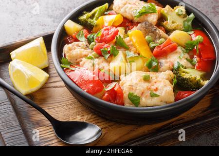 Stufato di pesce dietetico con peperoni, patate, piselli, cipolle, broccoli e pomodori da vicino in una ciotola sul tavolo. Orizzontale Foto Stock