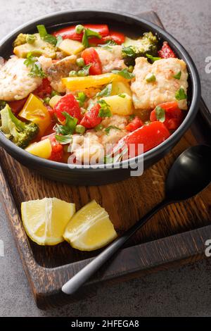 Stufato di pesce con verdure di stagione da vicino in una ciotola sul tavolo. Verticale. Stile mediterraneo Foto Stock