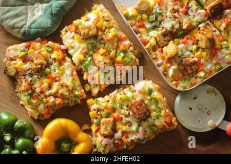 Fette rettangolari di pizza cotta in casa con paneer, mozzarella, peperoni verdi gialli rossi e cipolle. Cotto in un vassoio rettangolare Foto Stock