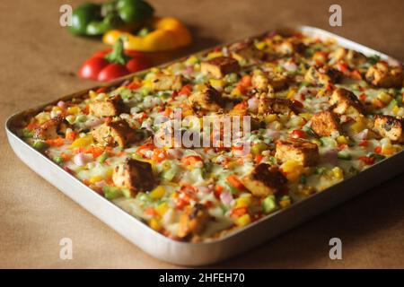 Pizza fatta in casa con paneer, mozzarella, peperoni rossi gialli verdi e cipolle. Cotto in un vassoio rettangolare Foto Stock