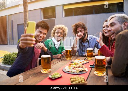 gruppo di amici multirazziali che prendono selfie sorridenti. con smartphone. Persone che si divertono all'aperto. Foto Stock