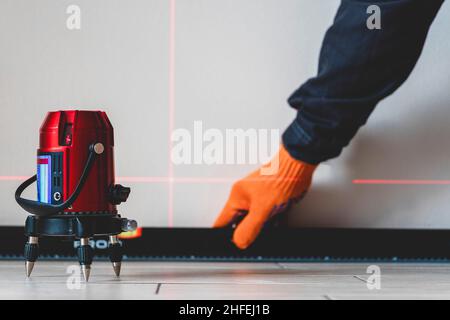 Operaio e bolla, livella laser. Linee a parete. Misurazione con livella laser rossa. Concetto di precisione di misurazione, moderni dispositivi di misurazione Foto Stock