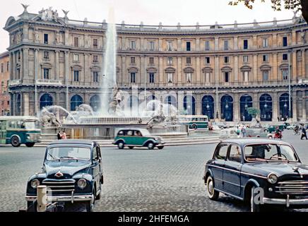 Il traffico passa per la Fontana delle Naiadi a Roma, Italia c.1960. La fontana (Fontana delle Naiadi) si trova al centro di Piazza della Repubblica sul colle Viminale. La fontana fu creata dall'architetto Alessandro Guerrieri nel 1888. Le sue quattro sculture in bronzo di naiadi (ninfe d'acqua della mitologia greco-romana classica) furono create dallo scultore Mario Rutelli e aggiunte nel 1901 – la scultura centrale del dio Glaucus di Rutelli fu aggiunta nel 1912 prima che la fontana fosse riinaugurata nel 1914. Questa immagine è da una trasparenza di colore 1950 amatoriale vintage 60s/35mm. Foto Stock