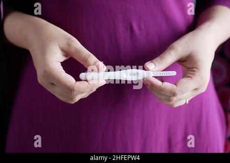 Donna tenuta a mano Kit di prova gravidanza su una scrivania in legno. Foto Stock
