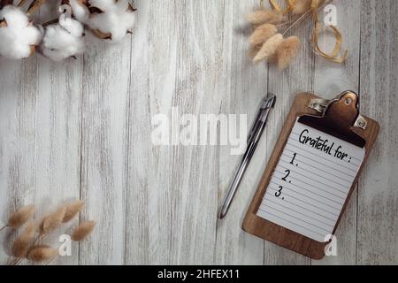 Riconoscente per la lista di testo su blocco note con legno rustico grigio fondo piatto e elementi naturali. Thankful concetto motivazionale. Foto Stock
