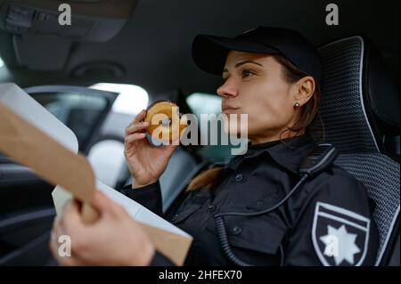 Donna poliziotto mangiare ciambella in auto Foto Stock