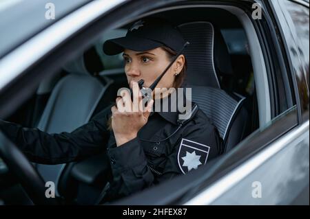 Poliziotto che usa la radio pattugliando strada in auto Foto Stock