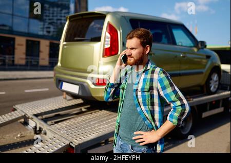 Uomo che chiama mentre traina il camion che preleva l'auto Foto Stock