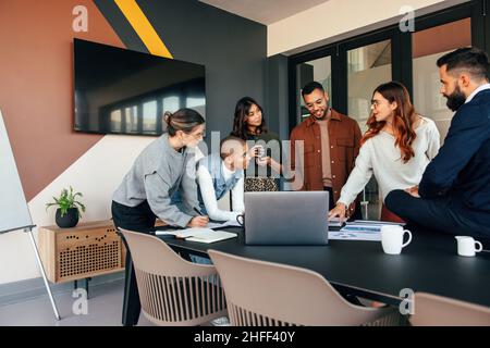 Diversi uomini d'affari che discutono di alcuni rapporti in una sala riunioni. Gruppo di uomini d'affari multiculturali in piedi intorno ad un tavolo in un ufficio moderno. Giovane Foto Stock