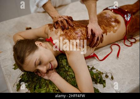 Giovane donna che ottiene il massaggio del miele nella sauna Foto Stock